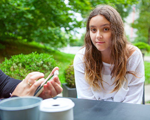 Parent with cell phone at table with female, teen with long, curly brown hair