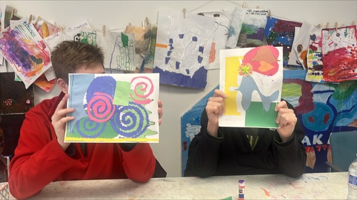 Two people holding their artwork in front of their faces