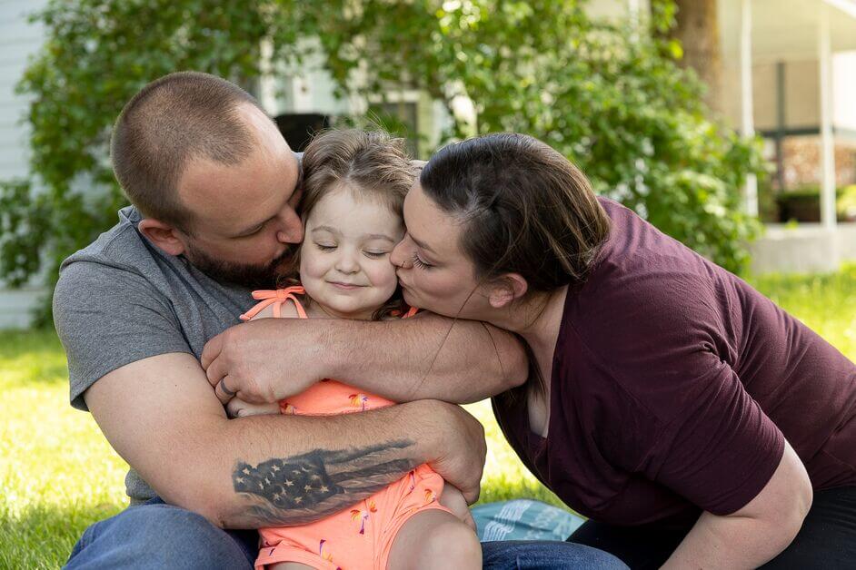 Little girl in pink dress being kissed by her parents on each cheek 