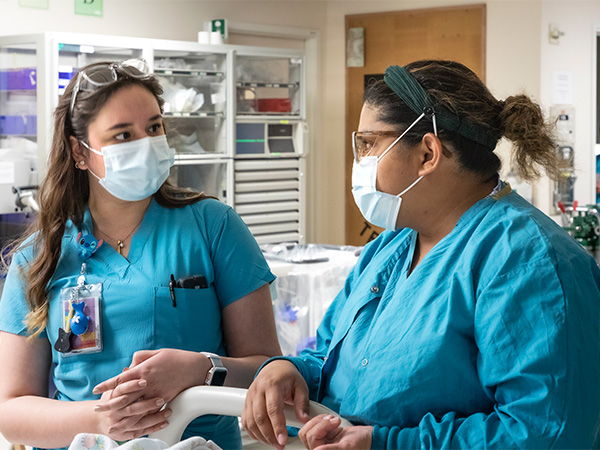 Two nurses coordinate care for their patient in a patient room