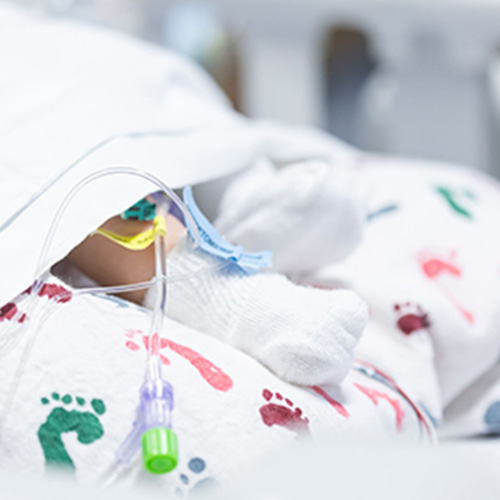 A closeup of a newborn baby's foot wearing a white sock sticks out between hospital blankets