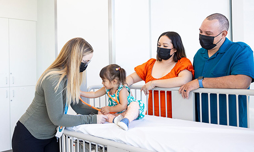 A female nurse looks over a young girl while her parents smile