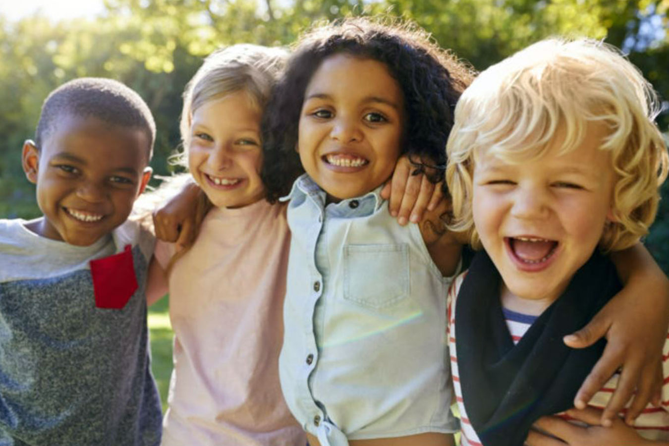 Four children smiling together on a sunny day