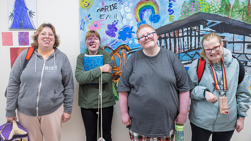 Four students stand in front of a mural created by ABC students. 