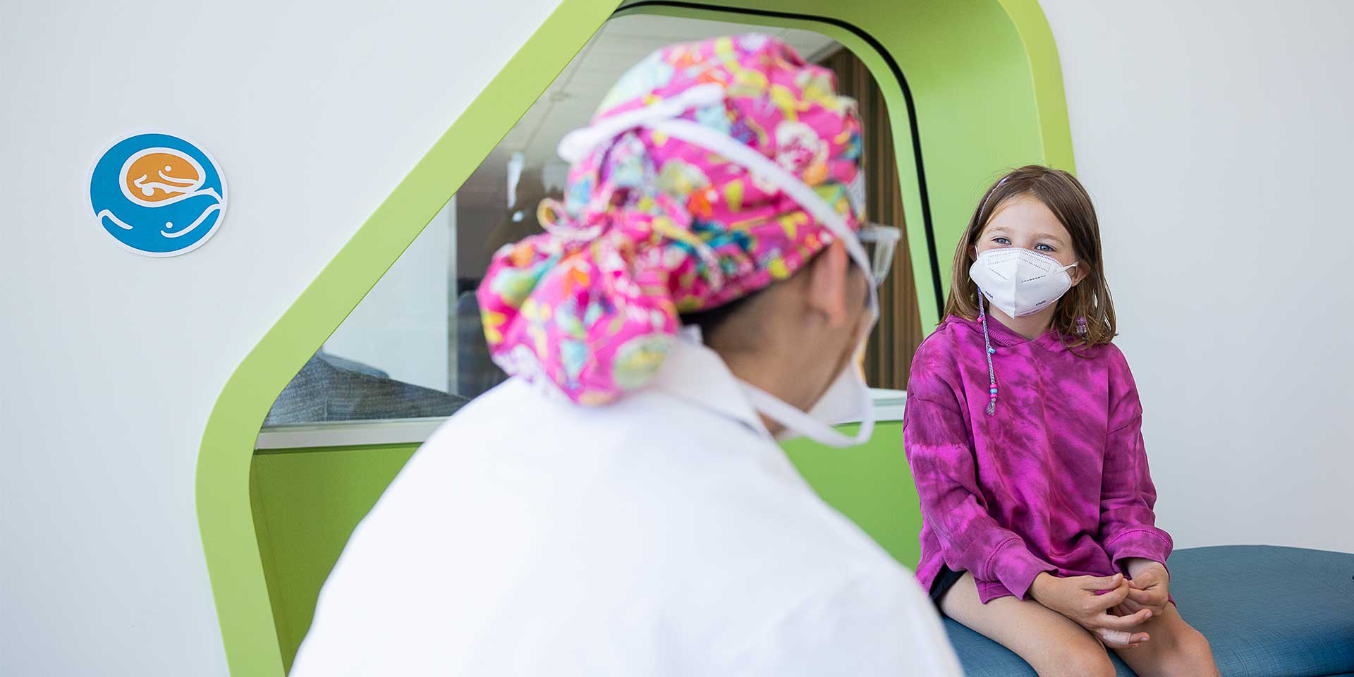 Seattle Children's patient in pink hoodie and mask talks with doctor