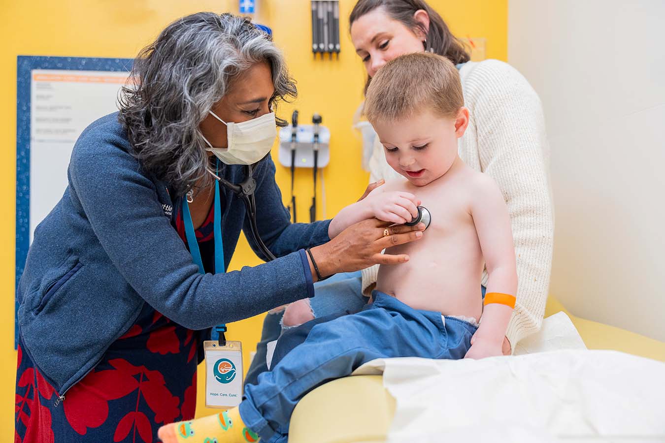 A doctor checks a boy's heart as he sits with his mother