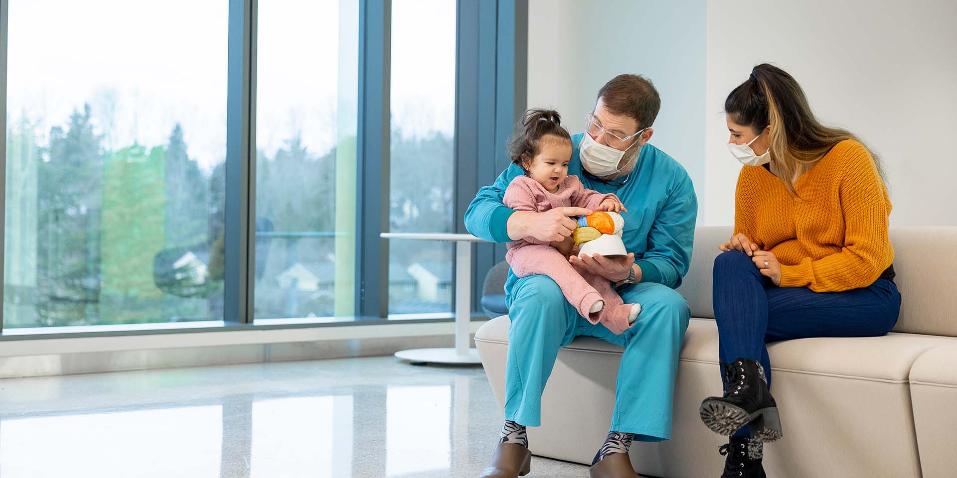 A girl sits in a doctor's lab and touches a model brain while her mother watches