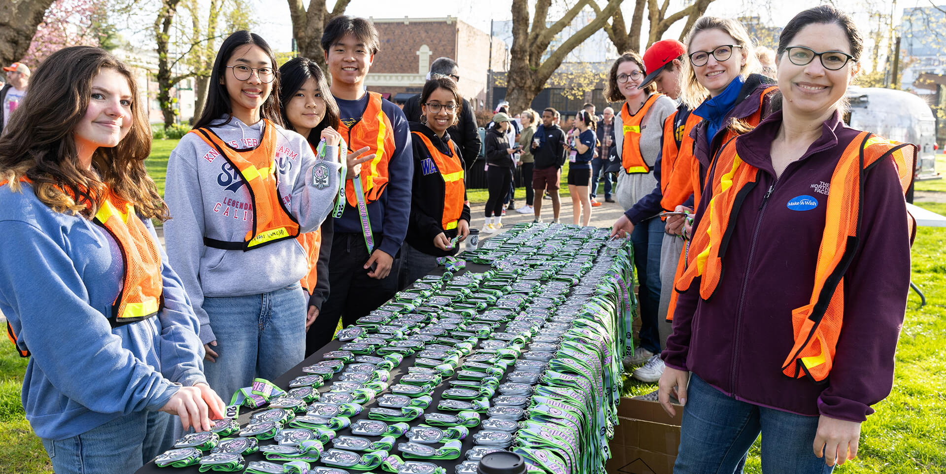 miling event volunteers in orange safety vests distributing race medals from a long table at an outdoor park