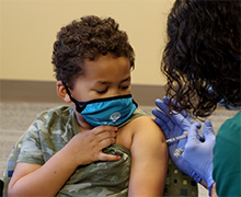 School aged boy watching a female administer his COVID-19 vaccine into his left arm