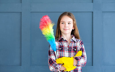 A girl in cleaning gloves holds a duster
