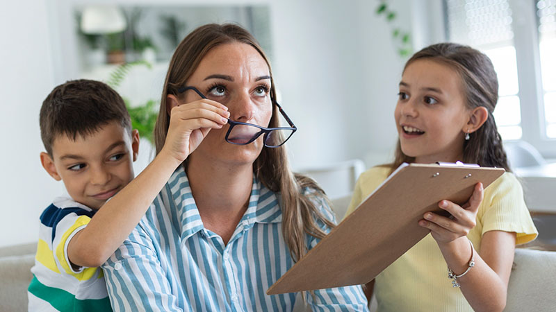 A mother looks frustrated as her kids play with her glasses and distract her from her work