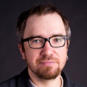 Martin Prlic, PhD, a fair-skinned man with short brown hair, a goatee, and black-rimmed glasses, looking directly at the camera against a dark background