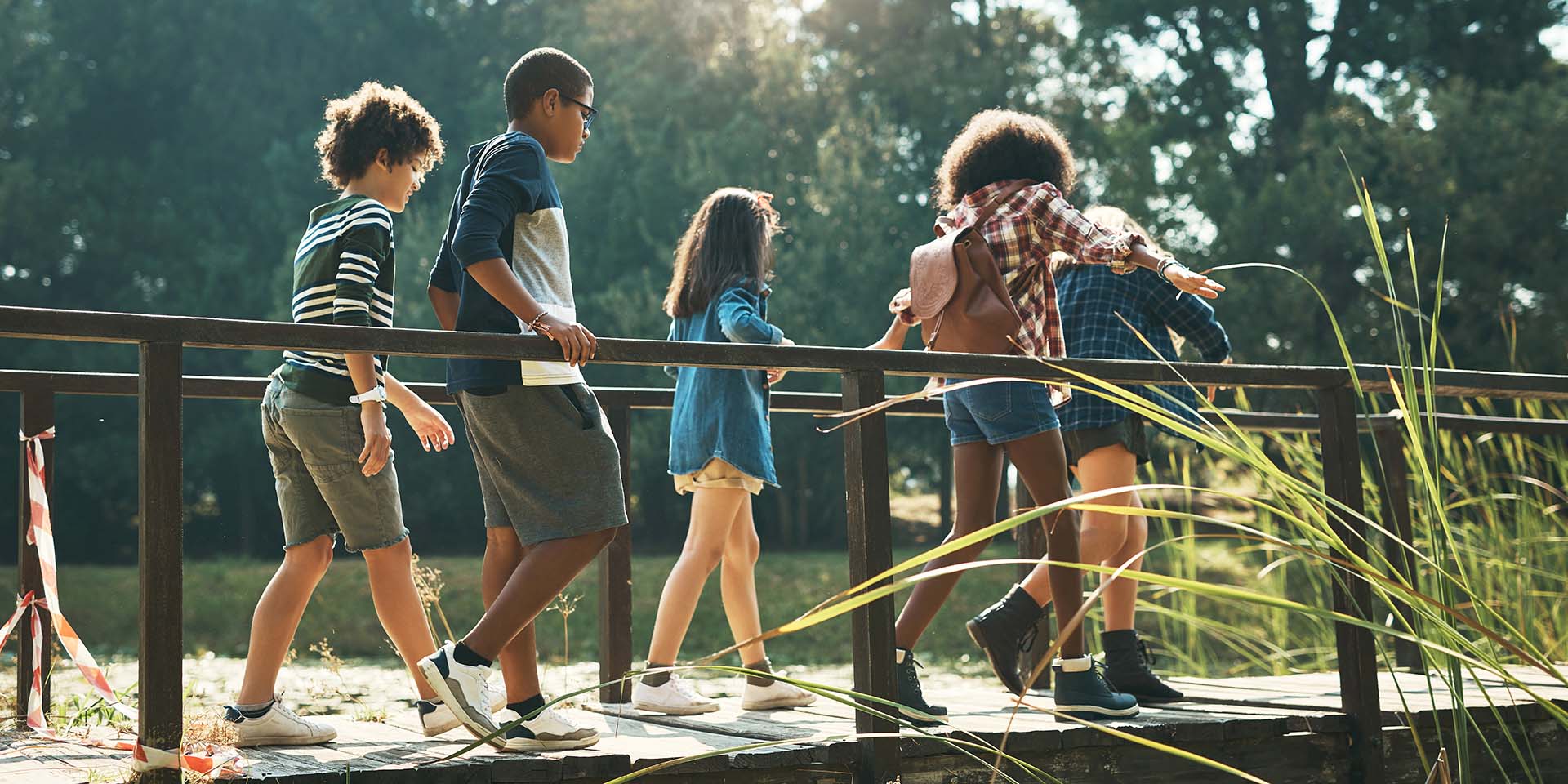 Five children walk across a wooden bridge on a sunny day