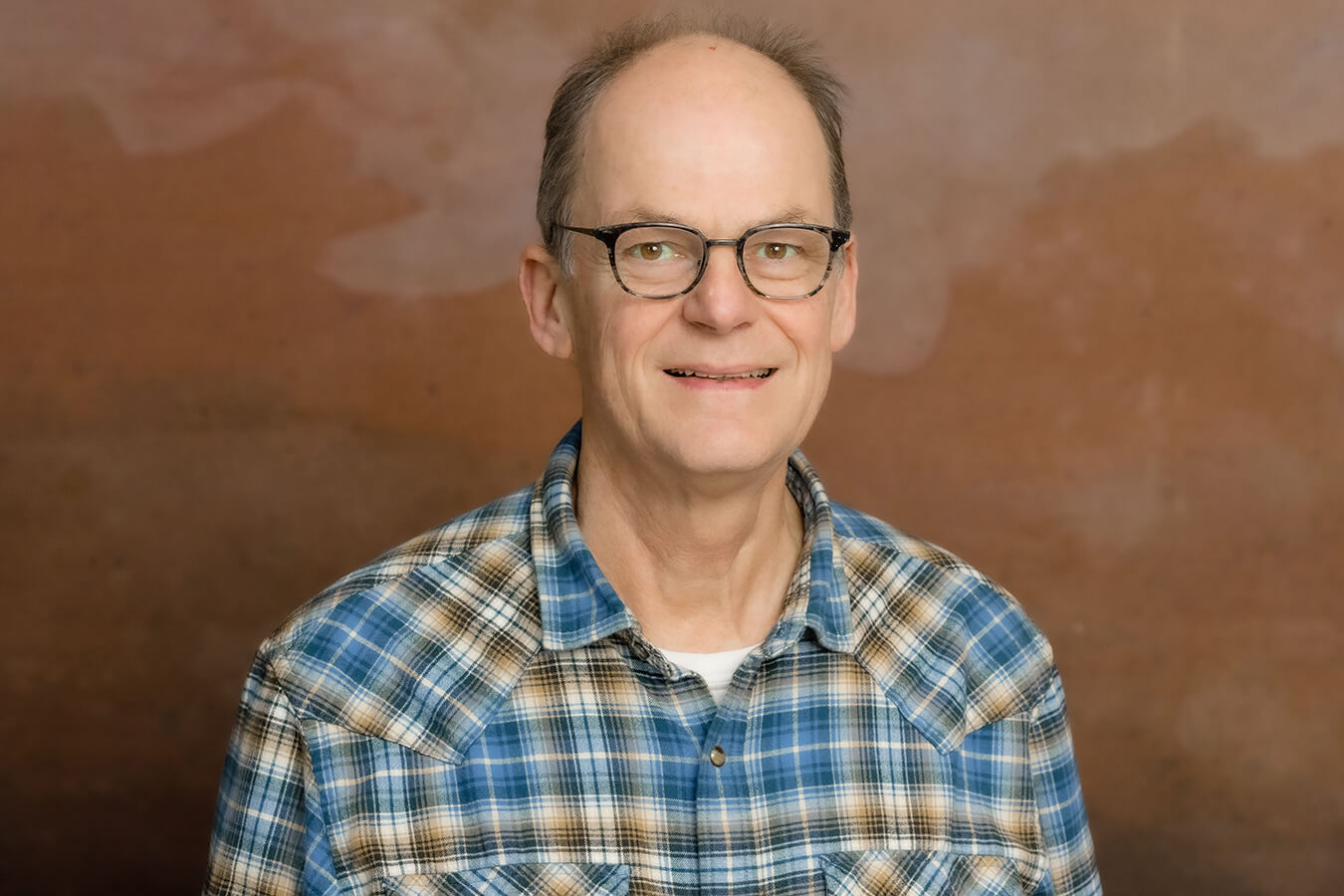 Headshot of researcher, Christian Roth, wearing glasses and a blue plaid shirt, smiling against a warm, brown background.