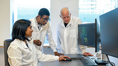 Invent scholars Drs. Sinduja Marx and Akinsola Oyelakin look at a computer screen with mentor Dr. Jim Olson