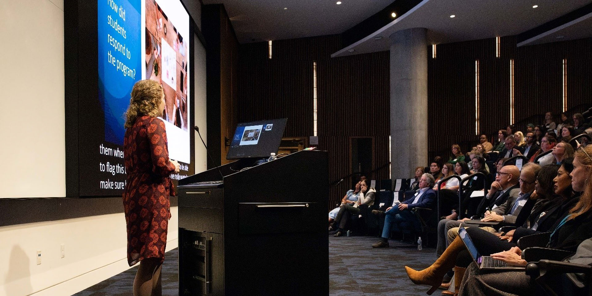 A woman speaks from a lecturn in front of an audience